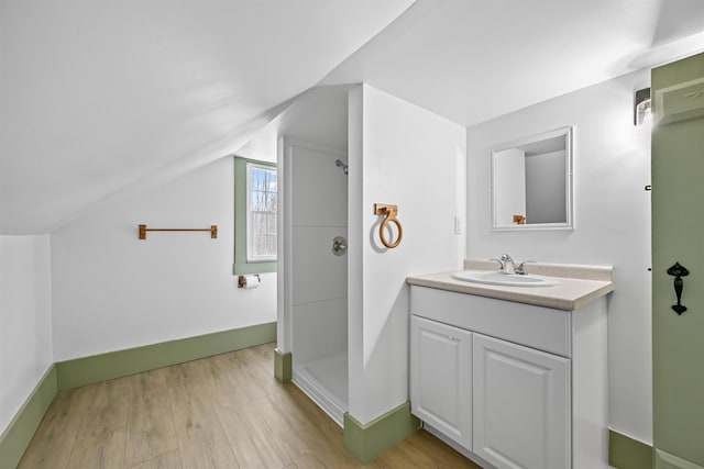 bathroom featuring lofted ceiling, wood finished floors, a shower, baseboards, and vanity