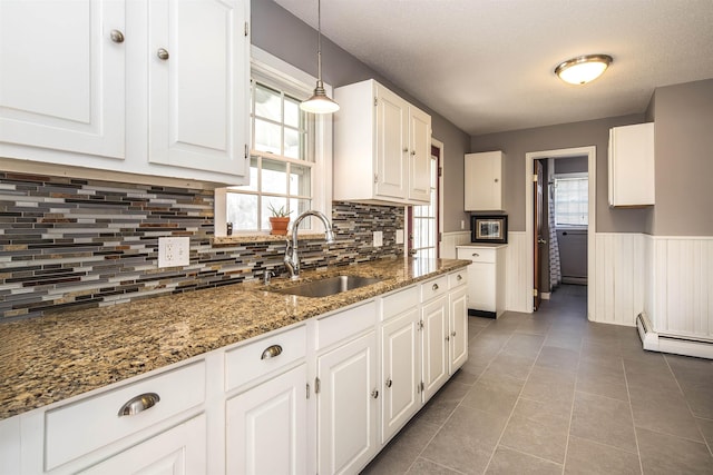 kitchen featuring a wainscoted wall, stone countertops, a sink, white cabinets, and baseboard heating