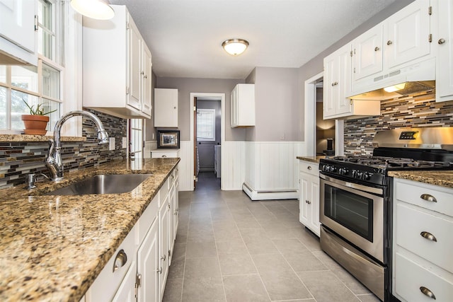 kitchen with a sink, under cabinet range hood, wainscoting, stainless steel gas stove, and baseboard heating