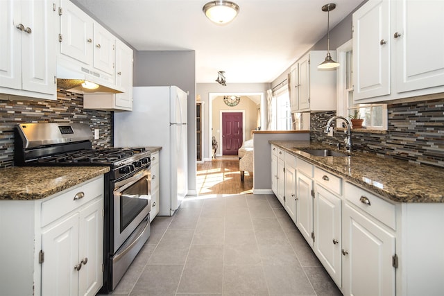 kitchen featuring a sink, decorative backsplash, white cabinets, under cabinet range hood, and stainless steel gas range oven