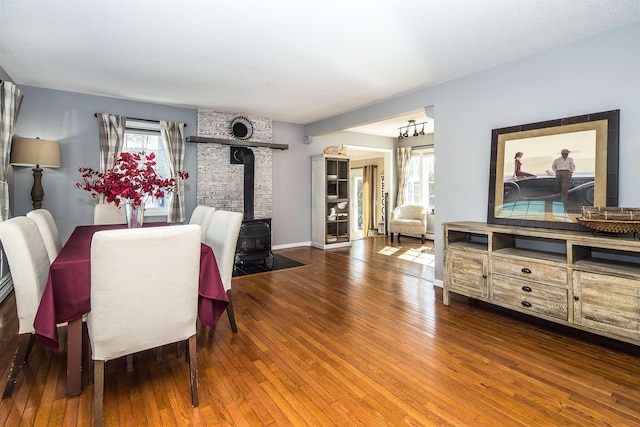 dining space featuring a wealth of natural light, baseboards, wood-type flooring, and a wood stove