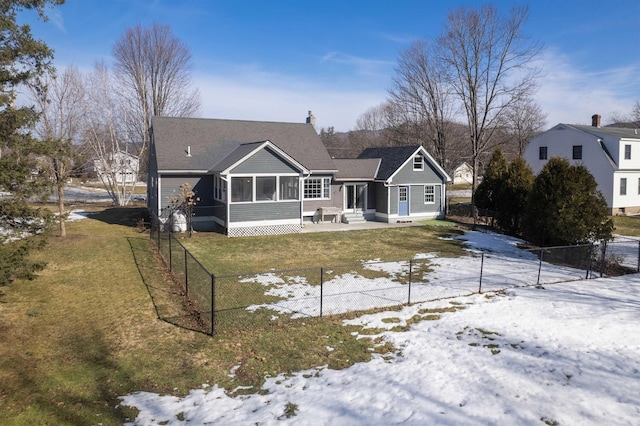 snow covered back of property featuring a patio area, fence, a lawn, and a sunroom