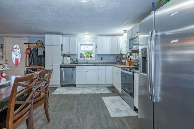 kitchen with dark wood-type flooring, a sink, a textured ceiling, appliances with stainless steel finishes, and white cabinets