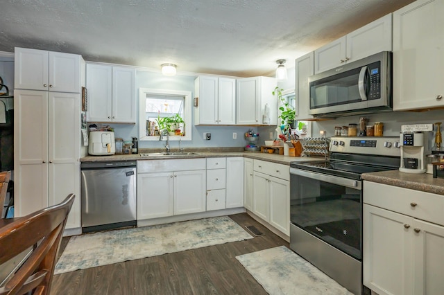 kitchen featuring visible vents, a sink, appliances with stainless steel finishes, white cabinets, and dark wood-style flooring