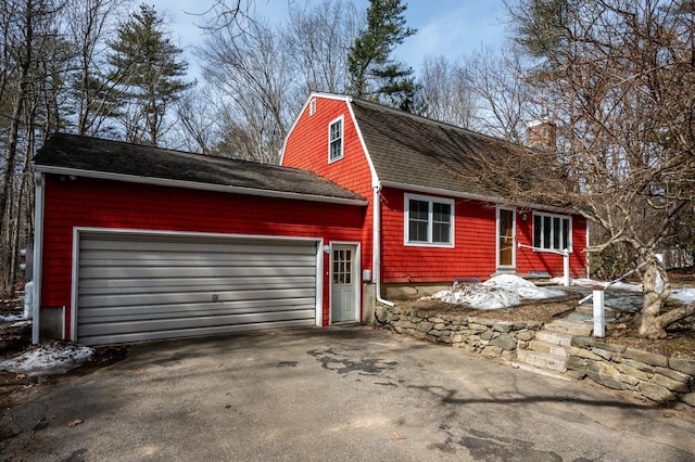 view of front of house featuring aphalt driveway, a gambrel roof, roof with shingles, and an attached garage