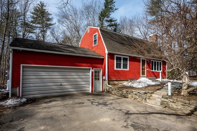 view of front of house featuring aphalt driveway, a gambrel roof, roof with shingles, and an attached garage