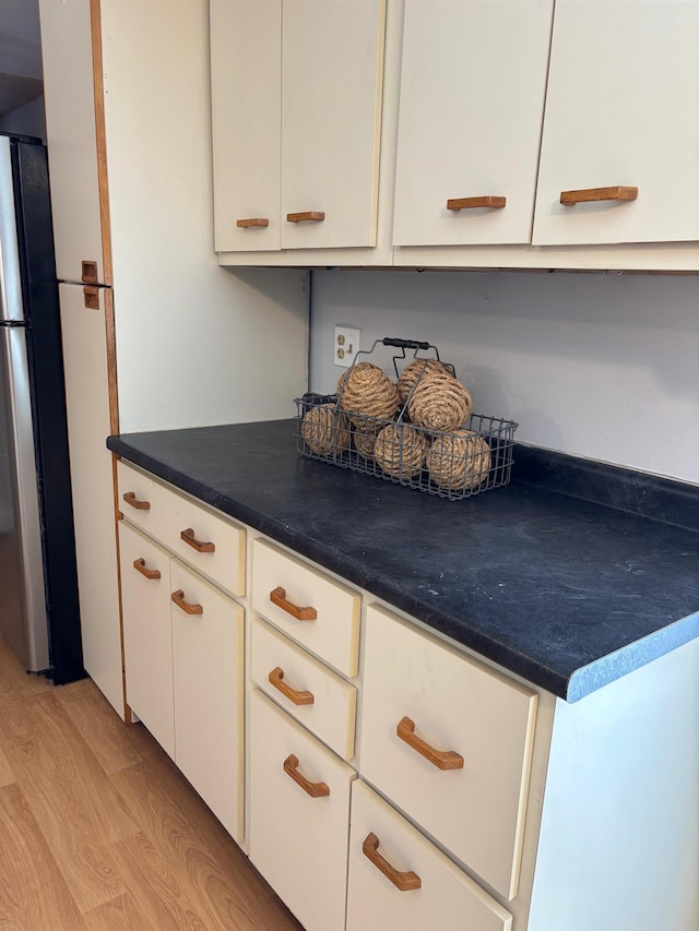 kitchen featuring light wood-type flooring, dark countertops, white cabinets, and freestanding refrigerator