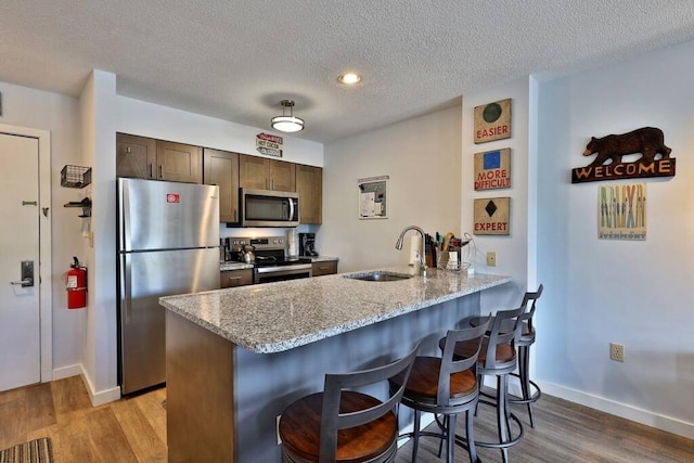 kitchen with light wood finished floors, a breakfast bar, a peninsula, stainless steel appliances, and a sink