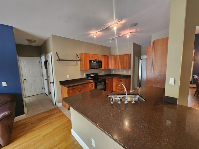 kitchen with brown cabinets, black appliances, a sink, light wood-style floors, and a peninsula