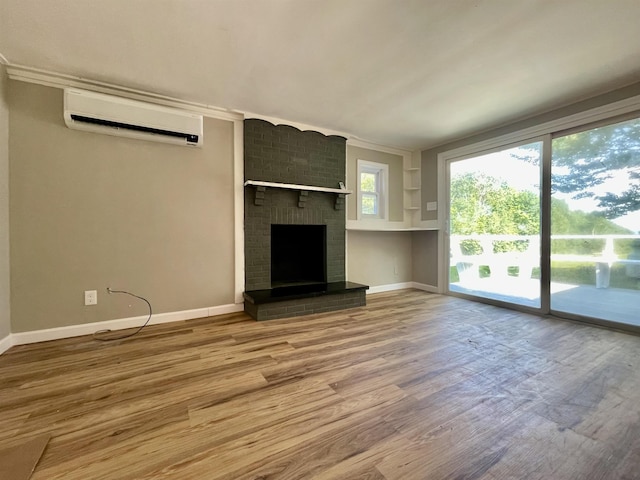 unfurnished living room with a brick fireplace, a wall mounted AC, baseboards, and wood finished floors