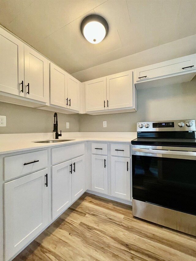 kitchen featuring electric range, a sink, light countertops, white cabinets, and light wood-style floors