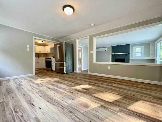 unfurnished living room with a sink, light wood-type flooring, baseboards, and crown molding
