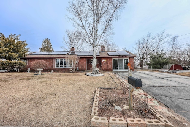 view of front of house with a front lawn, brick siding, roof mounted solar panels, and a chimney