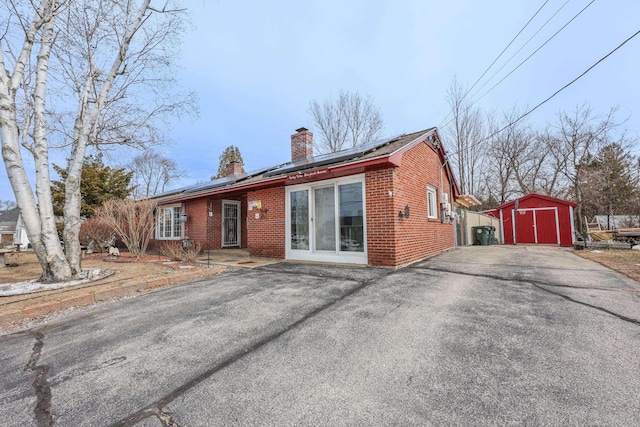 rear view of property with a storage shed, an outdoor structure, brick siding, and a chimney