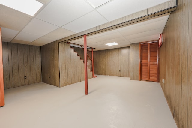 finished basement with stairway, wooden walls, and a drop ceiling