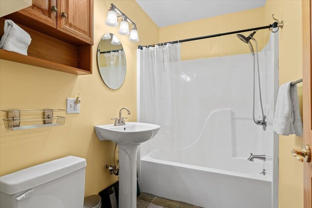 bathroom with toilet, shower / tub combo with curtain, and a sink