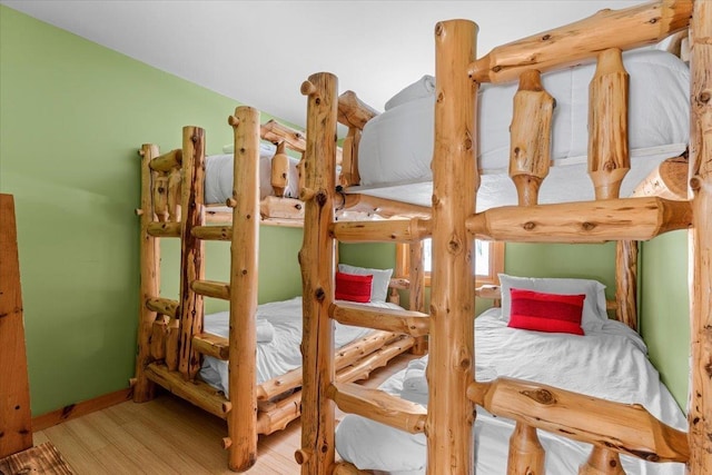 bedroom with log walls, baseboards, and wood finished floors