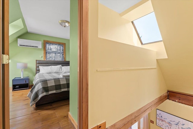 interior space featuring lofted ceiling with skylight, a wall mounted air conditioner, baseboards, and hardwood / wood-style flooring