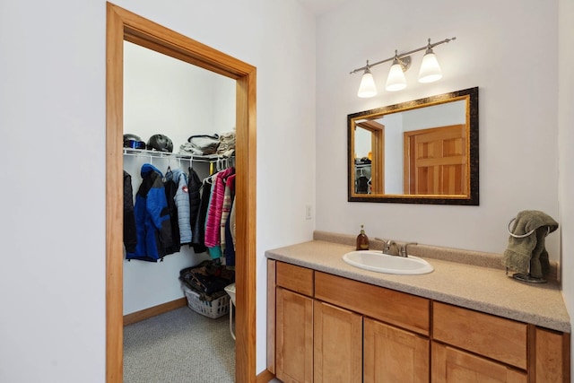 bathroom featuring a walk in closet, baseboards, and vanity