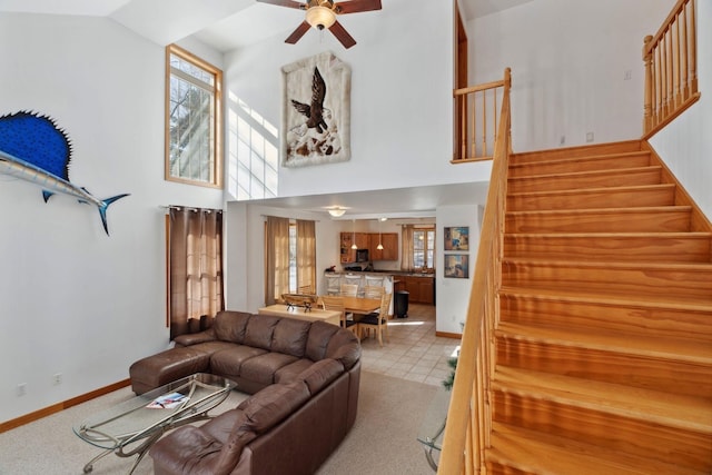 living area with stairway, baseboards, a high ceiling, and ceiling fan