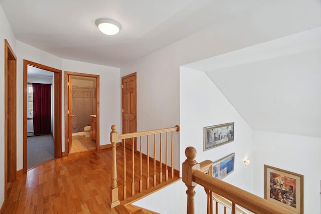 corridor with an upstairs landing, light wood-style flooring, and baseboards