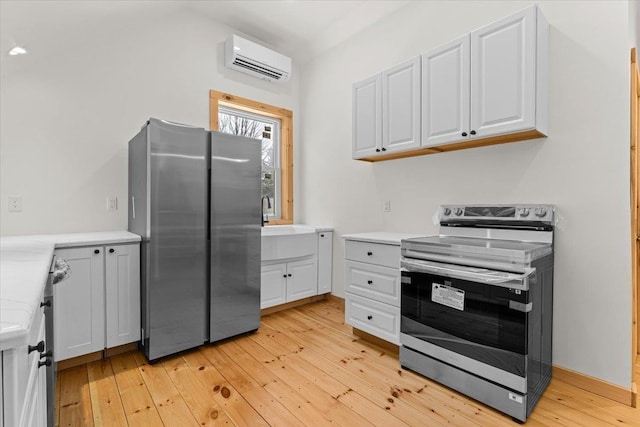 kitchen with a wall unit AC, light wood finished floors, stainless steel appliances, light countertops, and white cabinetry