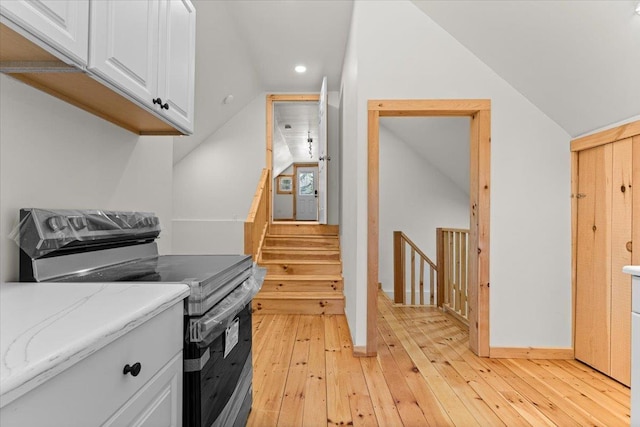 interior space featuring light wood-type flooring, lofted ceiling, recessed lighting, stainless steel range with electric stovetop, and white cabinetry