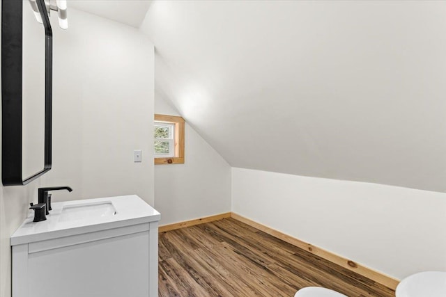 bathroom featuring toilet, wood finished floors, baseboards, vanity, and vaulted ceiling