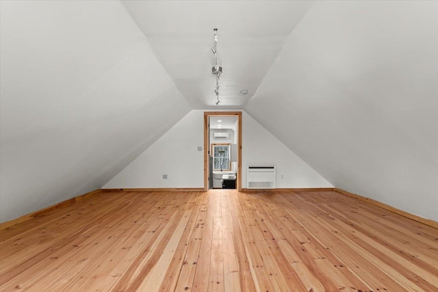 additional living space with heating unit, lofted ceiling, baseboards, and light wood finished floors