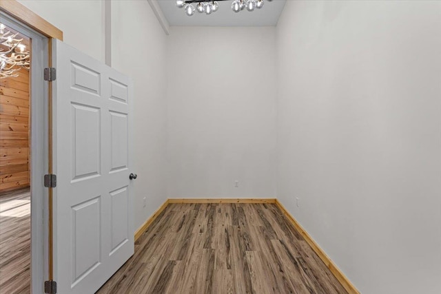 unfurnished room featuring baseboards, an inviting chandelier, and wood finished floors
