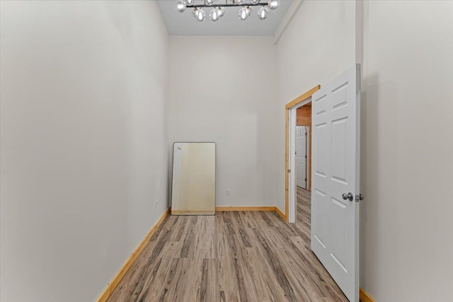 empty room featuring baseboards, light wood-type flooring, and a chandelier