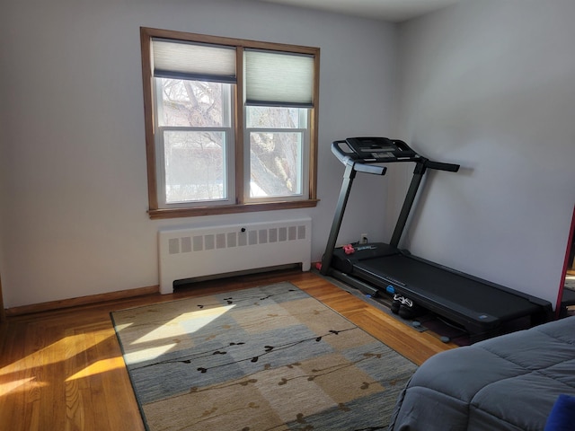 exercise area with radiator heating unit, wood finished floors, and baseboards