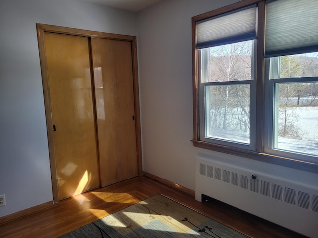 unfurnished bedroom featuring a closet, radiator, baseboards, and wood finished floors