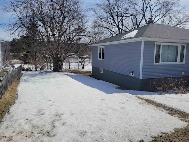 view of snowy exterior with a shingled roof, fence, and a chimney