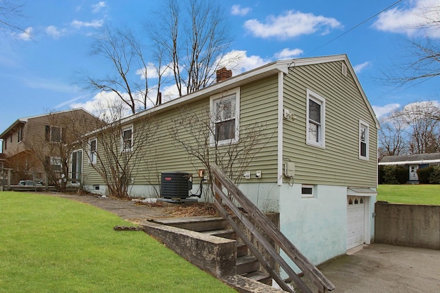 back of house with concrete driveway, central AC unit, a lawn, a chimney, and an attached garage