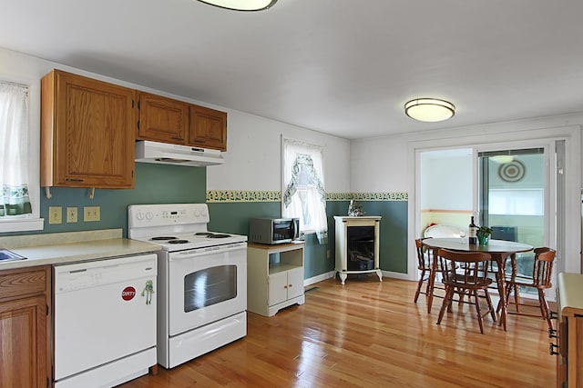 kitchen with white appliances, brown cabinetry, light countertops, under cabinet range hood, and light wood-type flooring