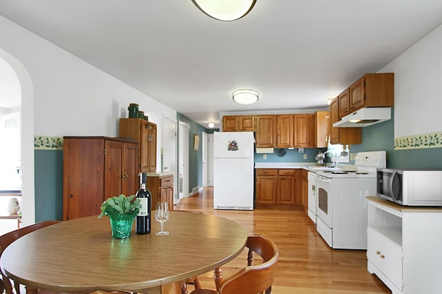 kitchen with light wood finished floors, under cabinet range hood, arched walkways, brown cabinetry, and white appliances