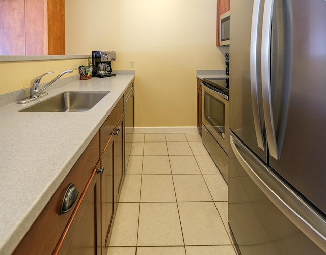 kitchen featuring baseboards, light countertops, appliances with stainless steel finishes, light tile patterned flooring, and a sink