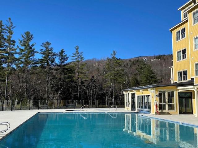 view of pool featuring a fenced in pool, a patio area, a wooded view, and fence