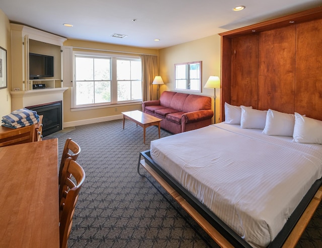 bedroom featuring visible vents, a fireplace with flush hearth, recessed lighting, dark colored carpet, and baseboards