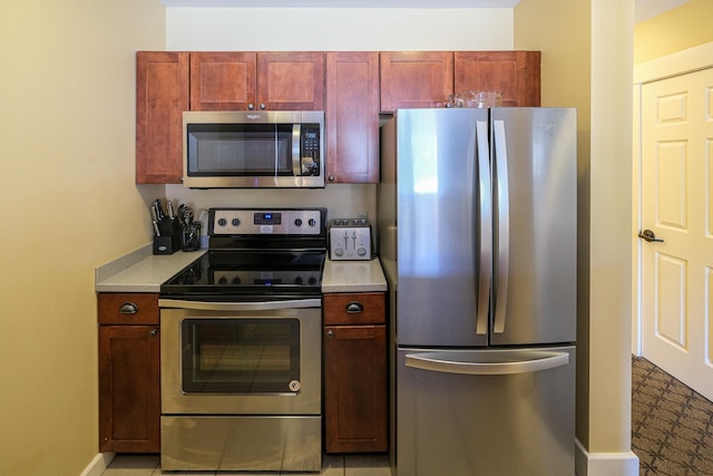 kitchen with light countertops, baseboards, reddish brown cabinets, and stainless steel appliances