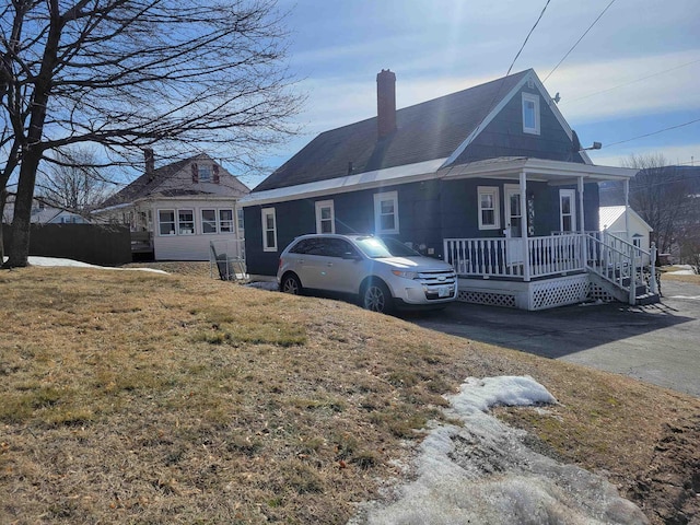 view of front of property with covered porch, a chimney, and a front yard