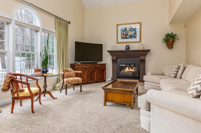 living area with a glass covered fireplace, plenty of natural light, baseboards, and carpet floors