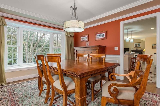 dining space with crown molding, wood finished floors, and a wainscoted wall