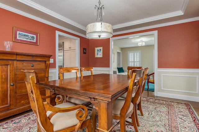 dining area with wood finished floors, a wainscoted wall, and ornamental molding