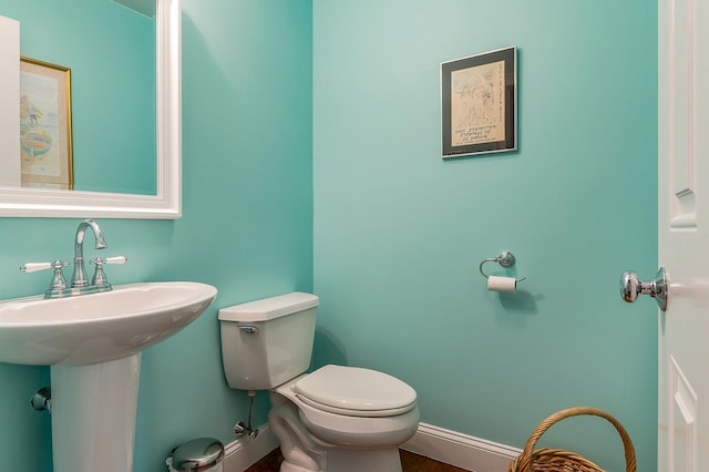 half bath with toilet, baseboards, and a sink