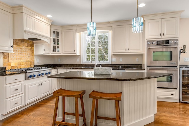 kitchen featuring a breakfast bar, a sink, hanging light fixtures, light wood-style floors, and appliances with stainless steel finishes