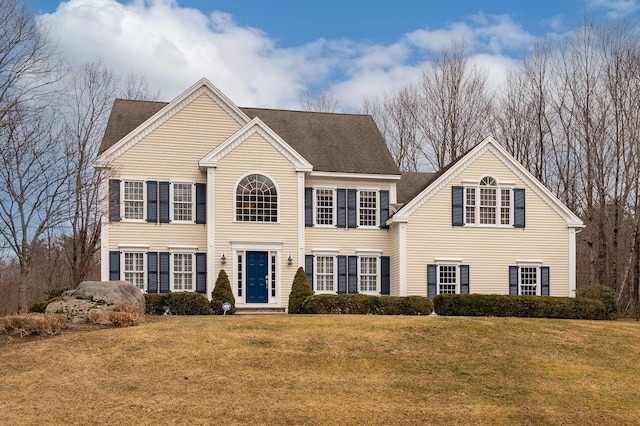 colonial home featuring a front yard and a shingled roof