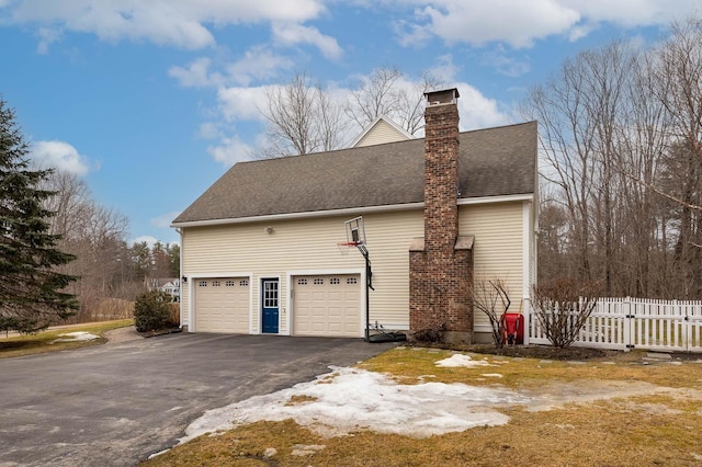 view of property exterior featuring a shingled roof, fence, aphalt driveway, a chimney, and an attached garage