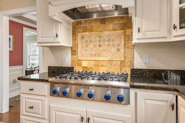 kitchen with a wainscoted wall, ornamental molding, custom range hood, white cabinetry, and stainless steel gas stovetop